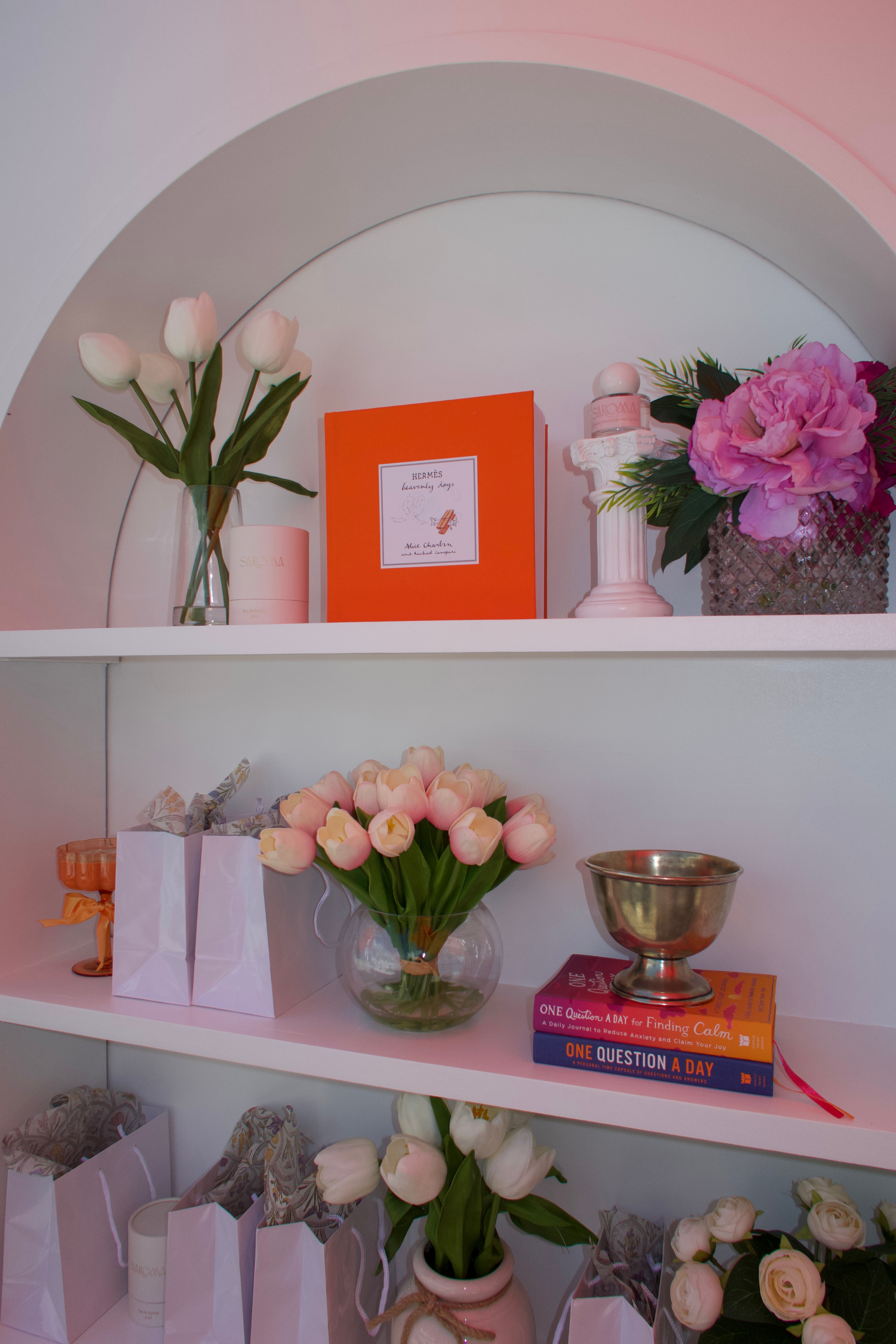 Shelves with pink flowers, a framed picture, books, and decorative items, arranged in a pastel-colored setting.