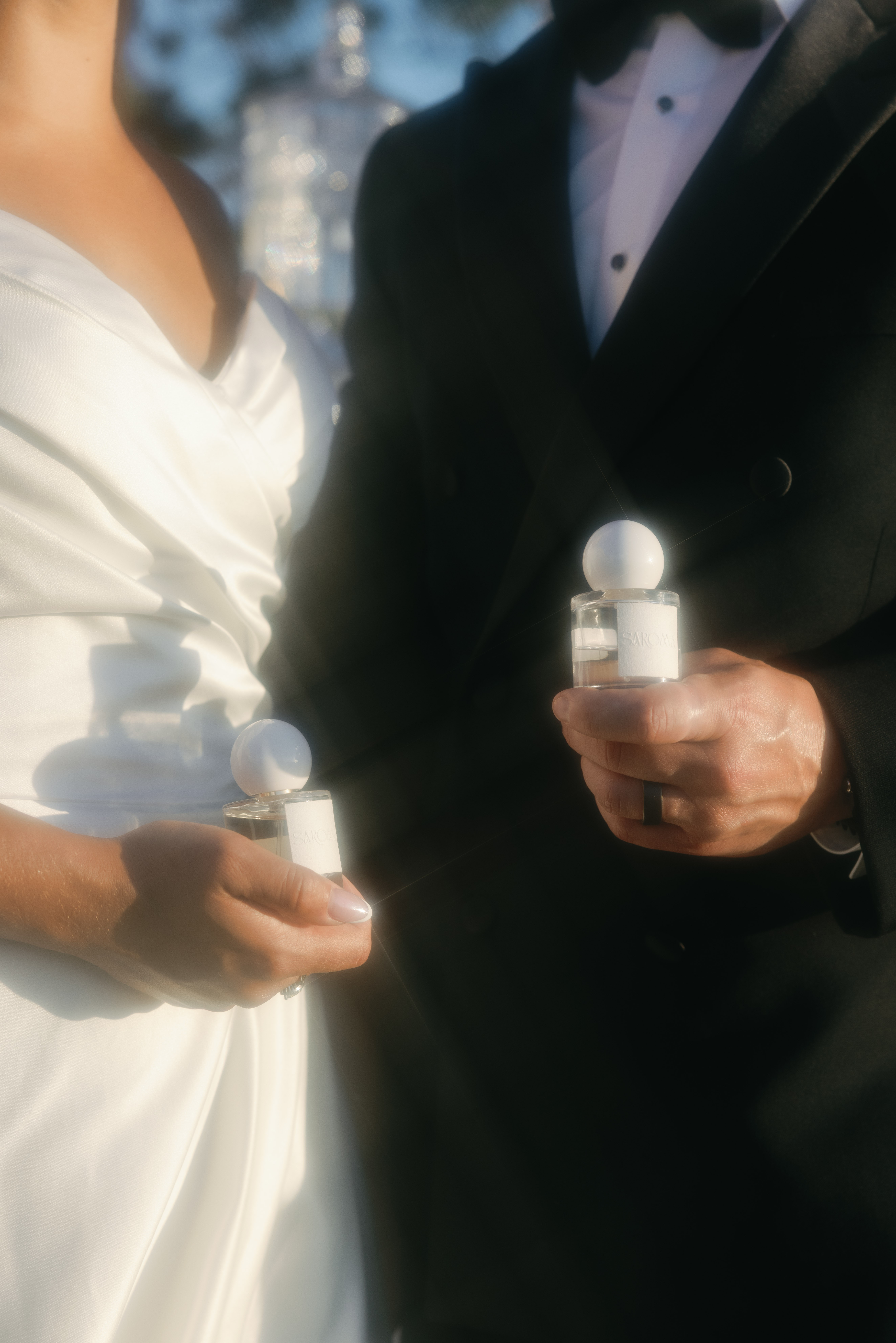 Close-up of a bride and groom holding candles during a wedding ceremony, with the bride in a white dress and the groom in a tuxedo.