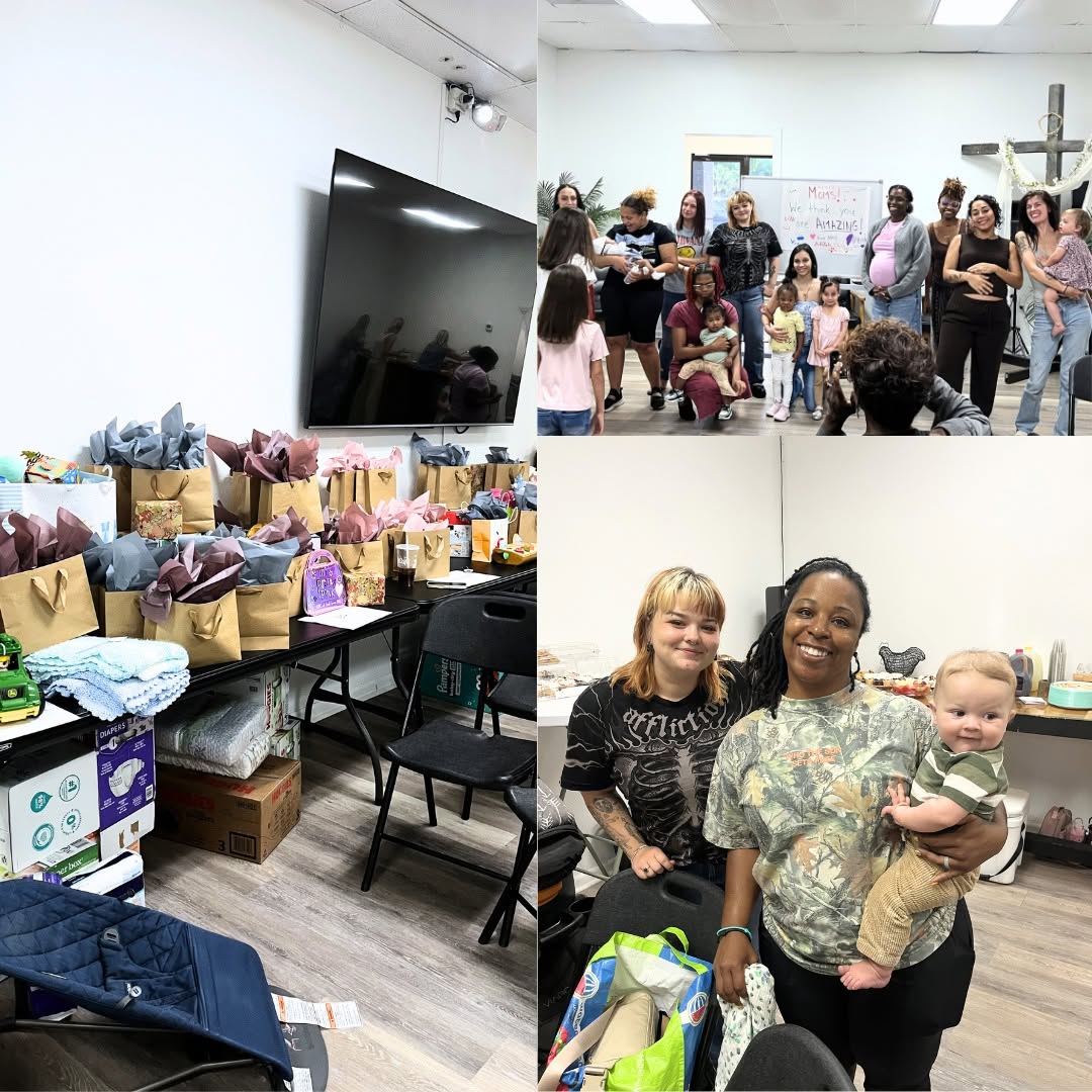 Group of people gathered in a room with a large TV, some sitting, some standing, and a woman holding a baby, with gift bags on a table.
