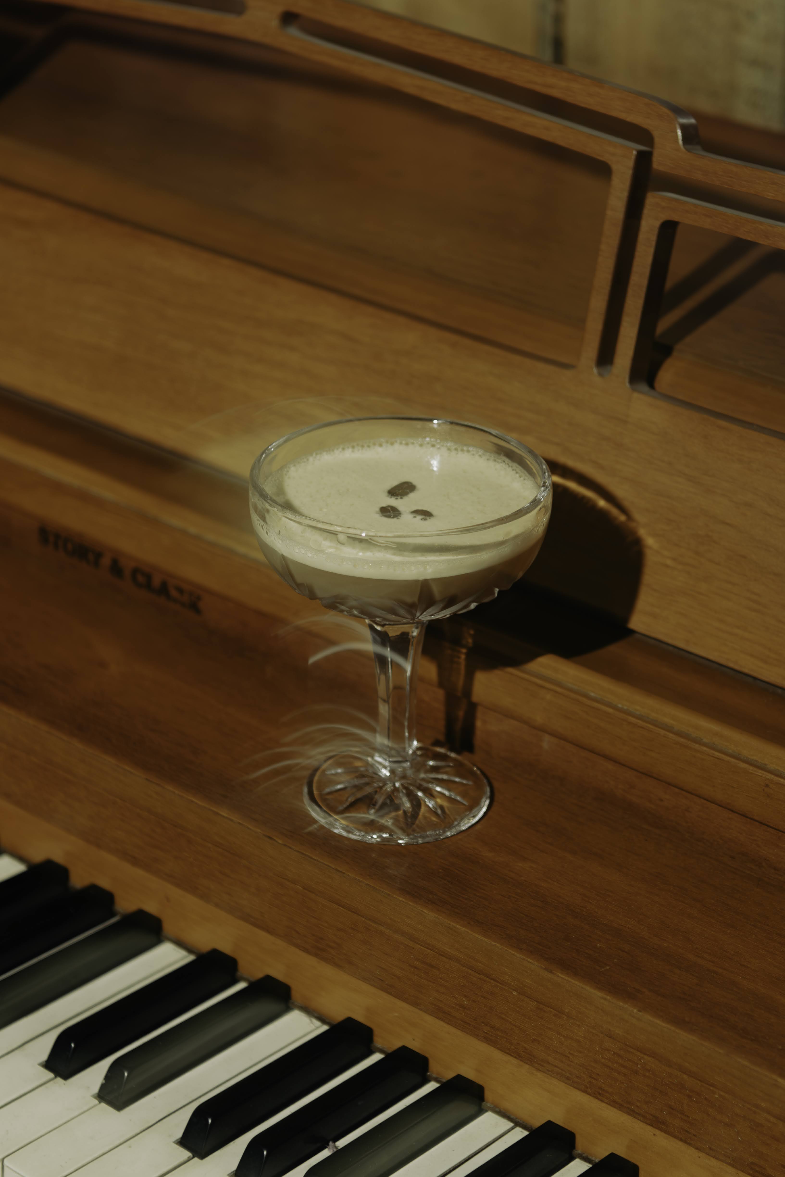A cocktail glass with a creamy drink on a wooden piano, with a wooden music stand in the background.