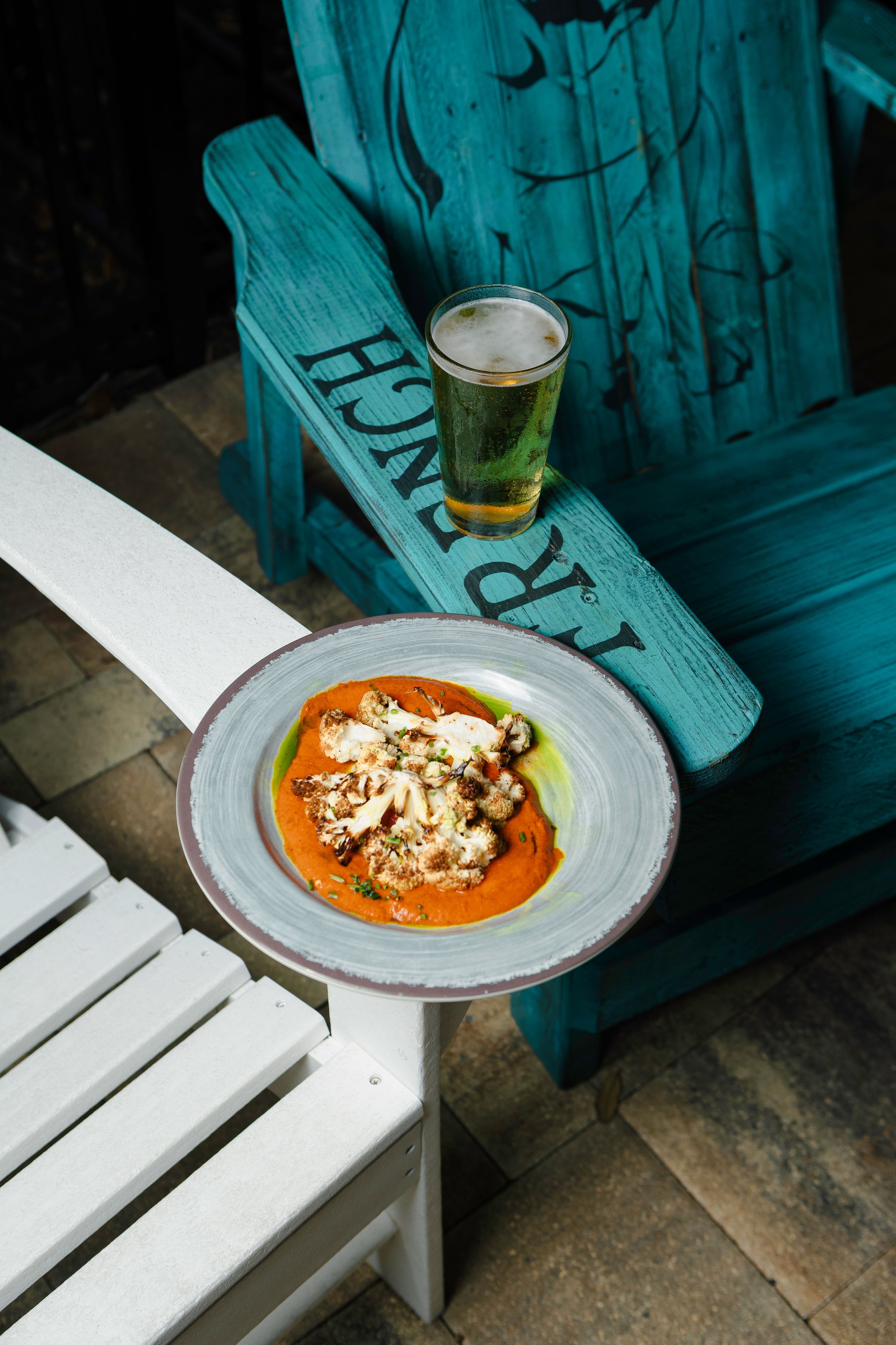 A plate with food and a glass of beer on a small white table next to a blue wooden bench.