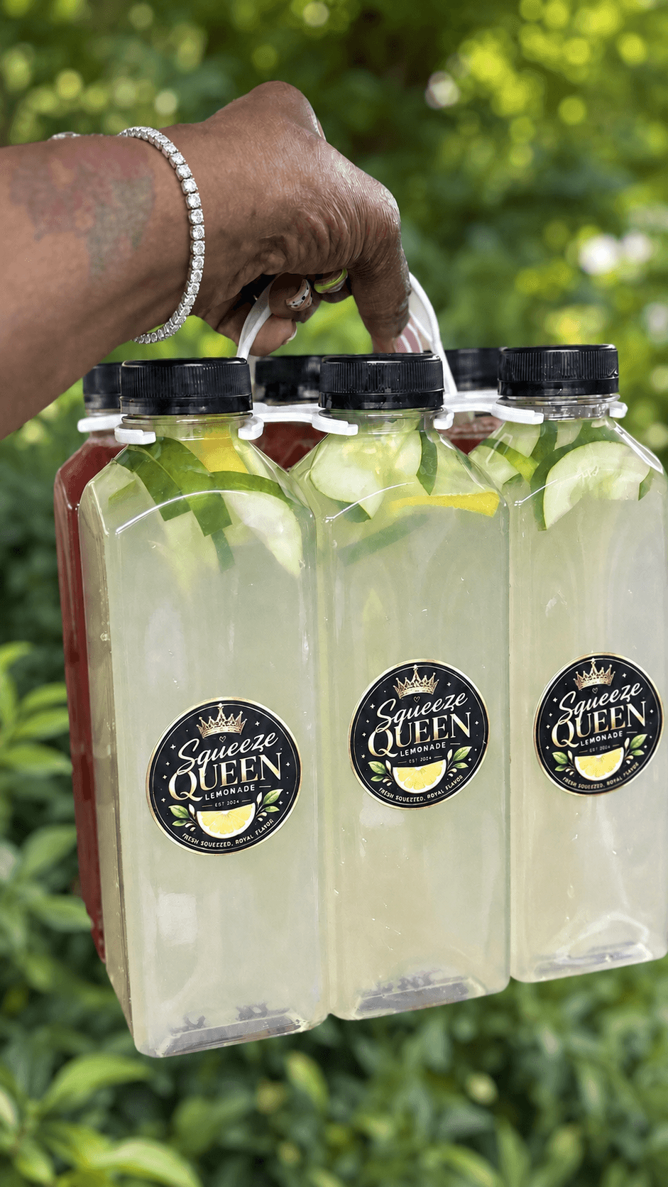 Hand holding a four-pack of bottled beverages with lemon slices, outdoors with green foliage background.