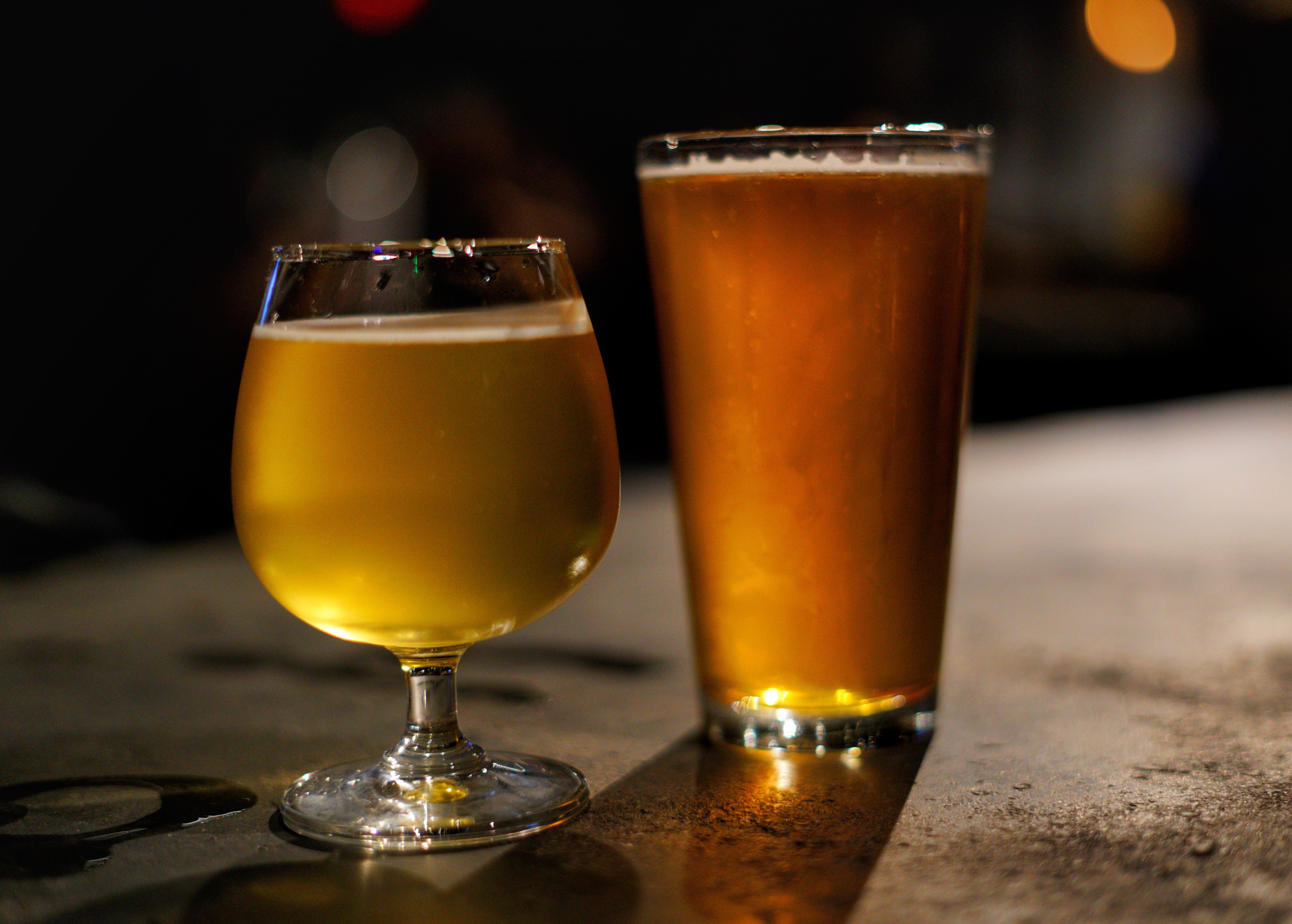 Two glasses of beer, one in a short glass and one in a tall glass, on a bar counter.