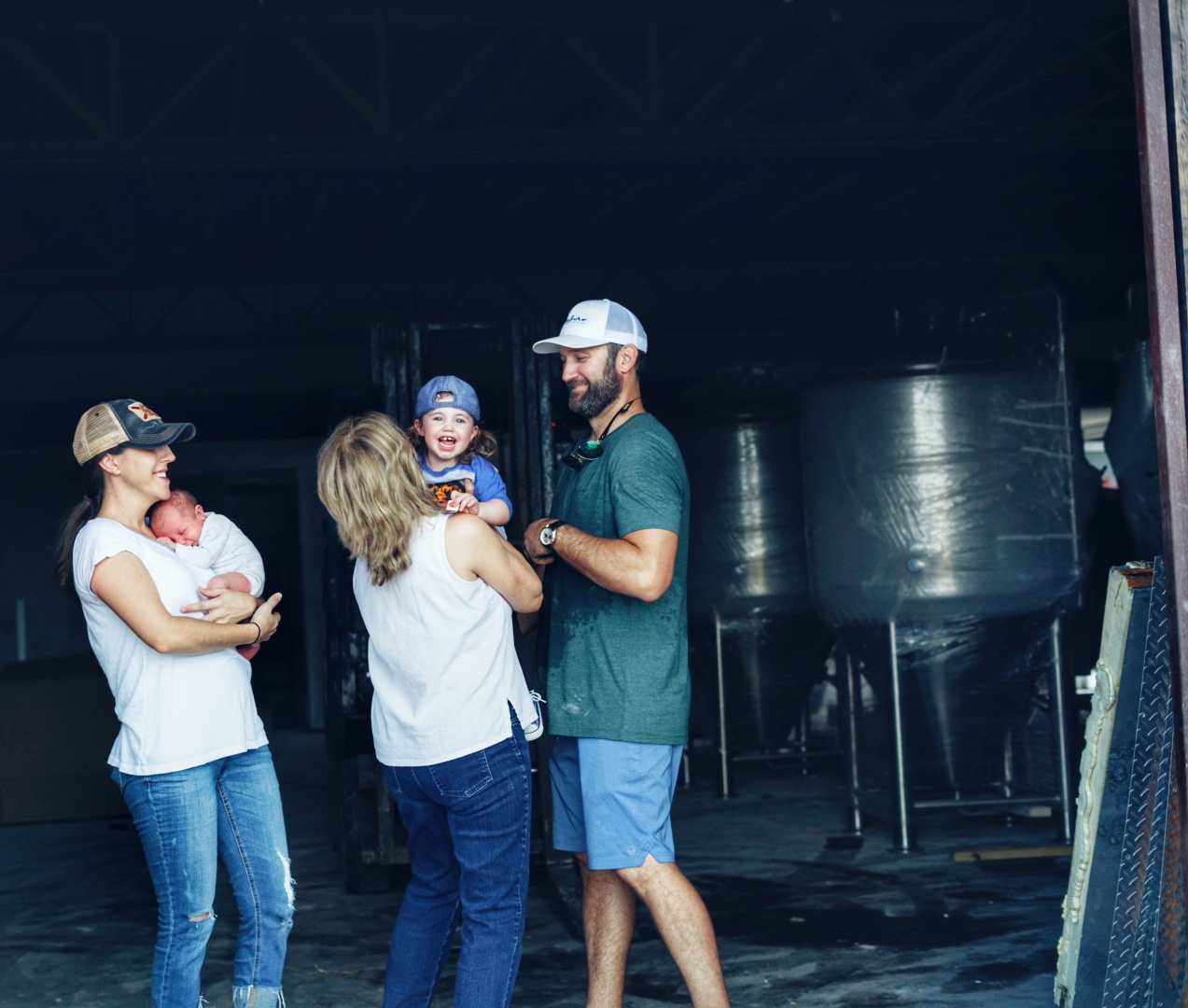 Group of five people, including children, standing and talking indoors, with a large metallic tank in the background.