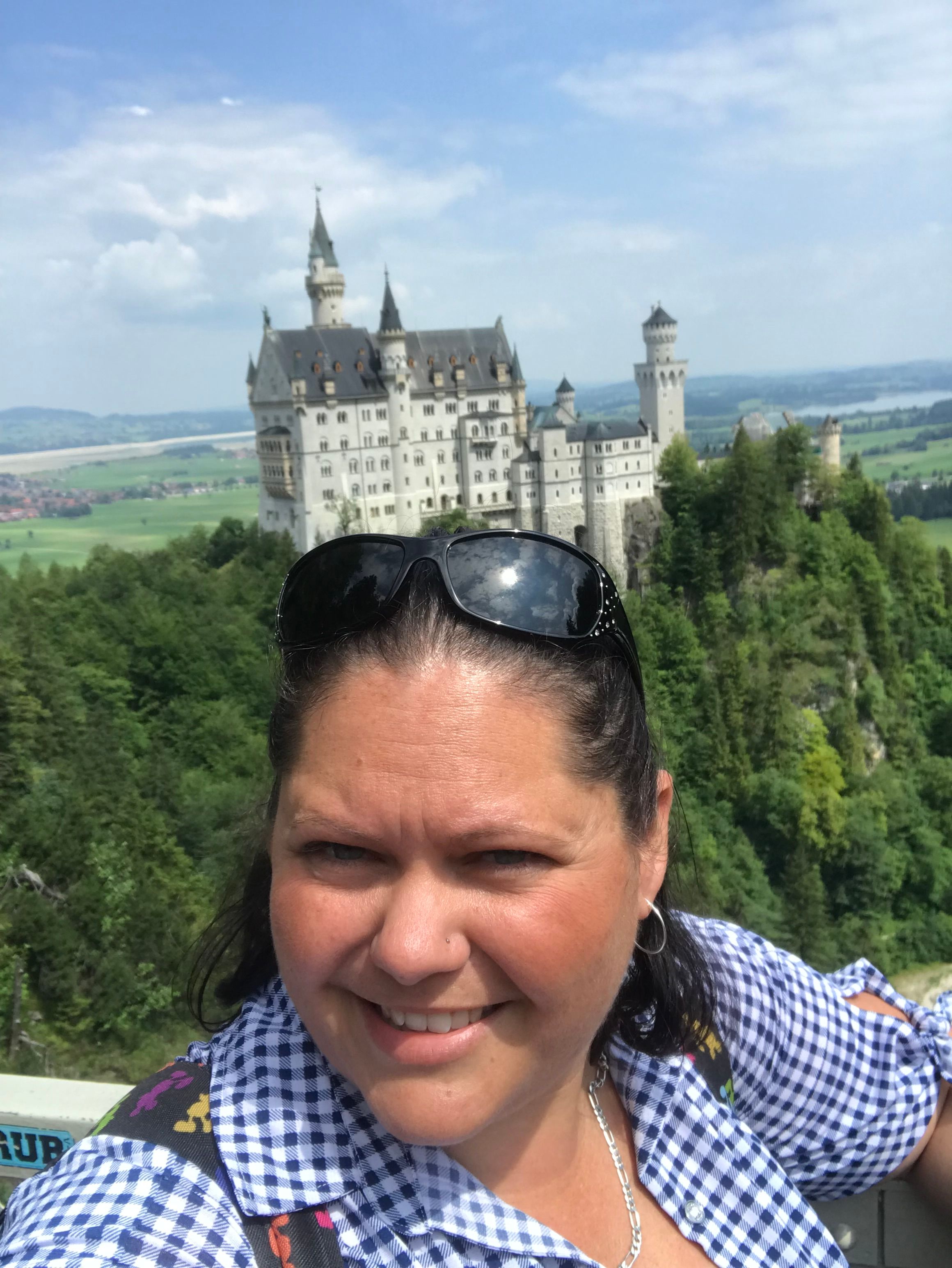 Woman taking a selfie with a castle and green landscape in the background, sunny day.