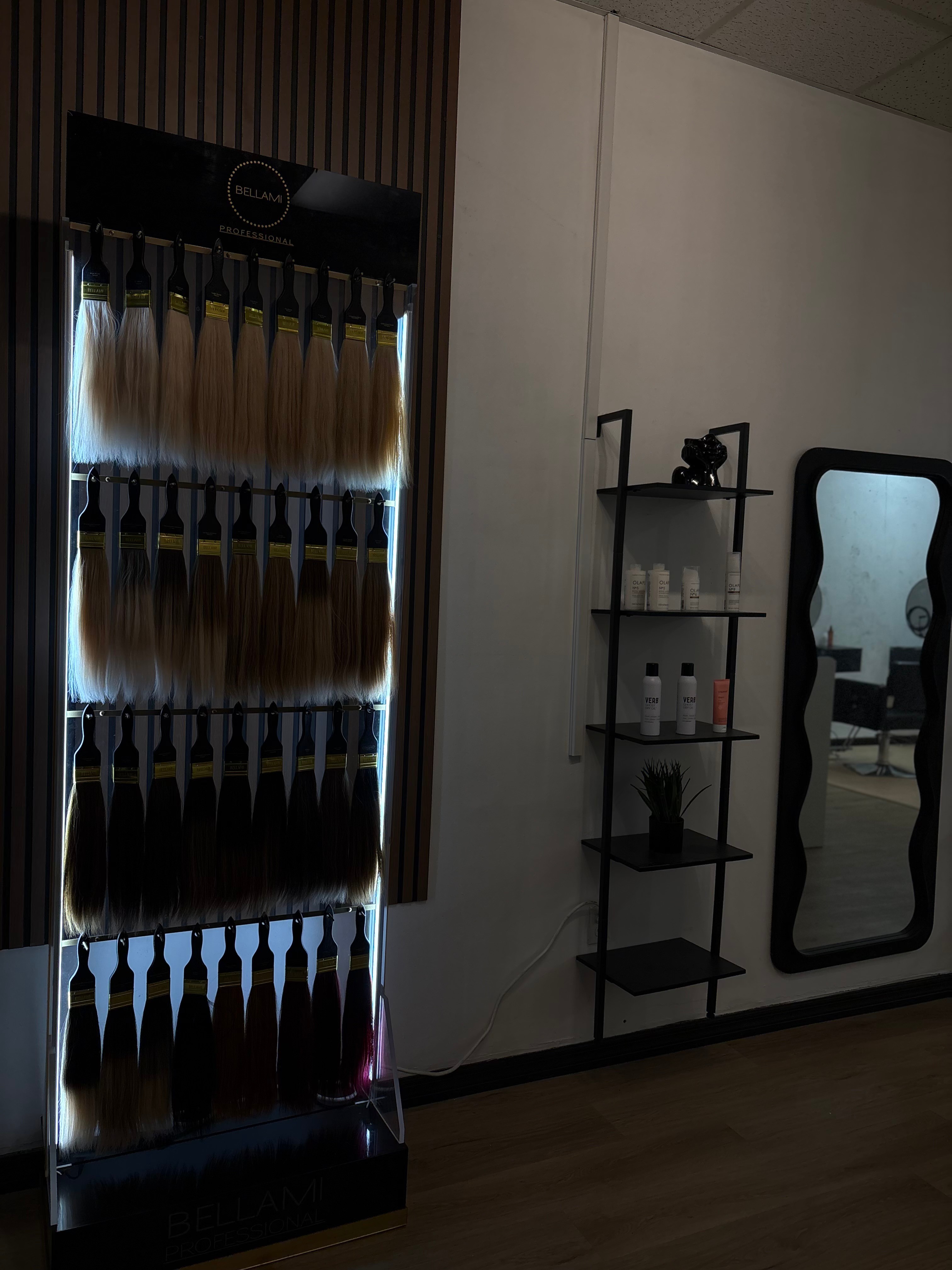 Display of hair color samples on a black stand, a mirror, and a black shelf with bottles and decor, in a salon.