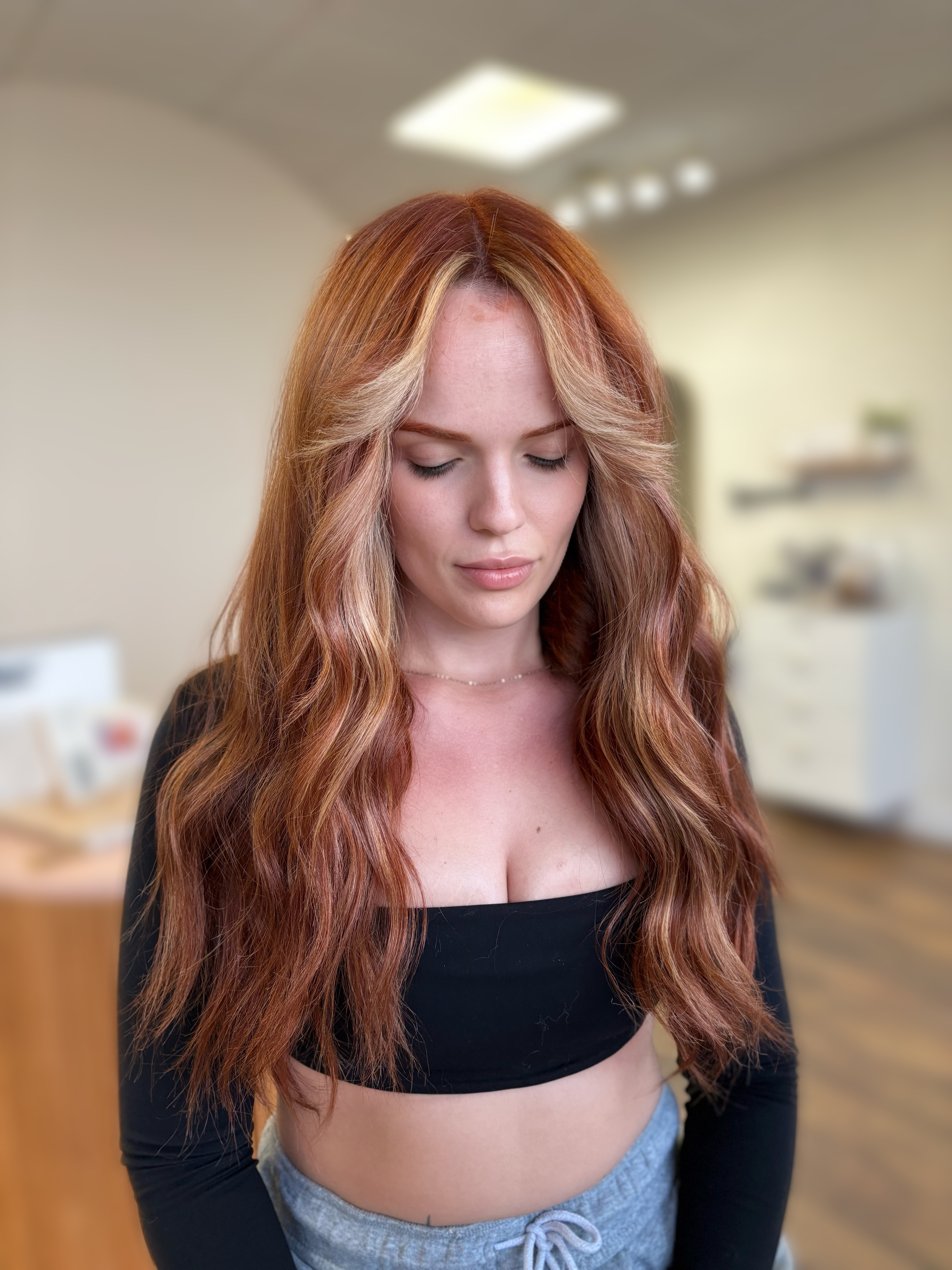 Young woman with long, wavy red hair looking downward in an indoor setting.