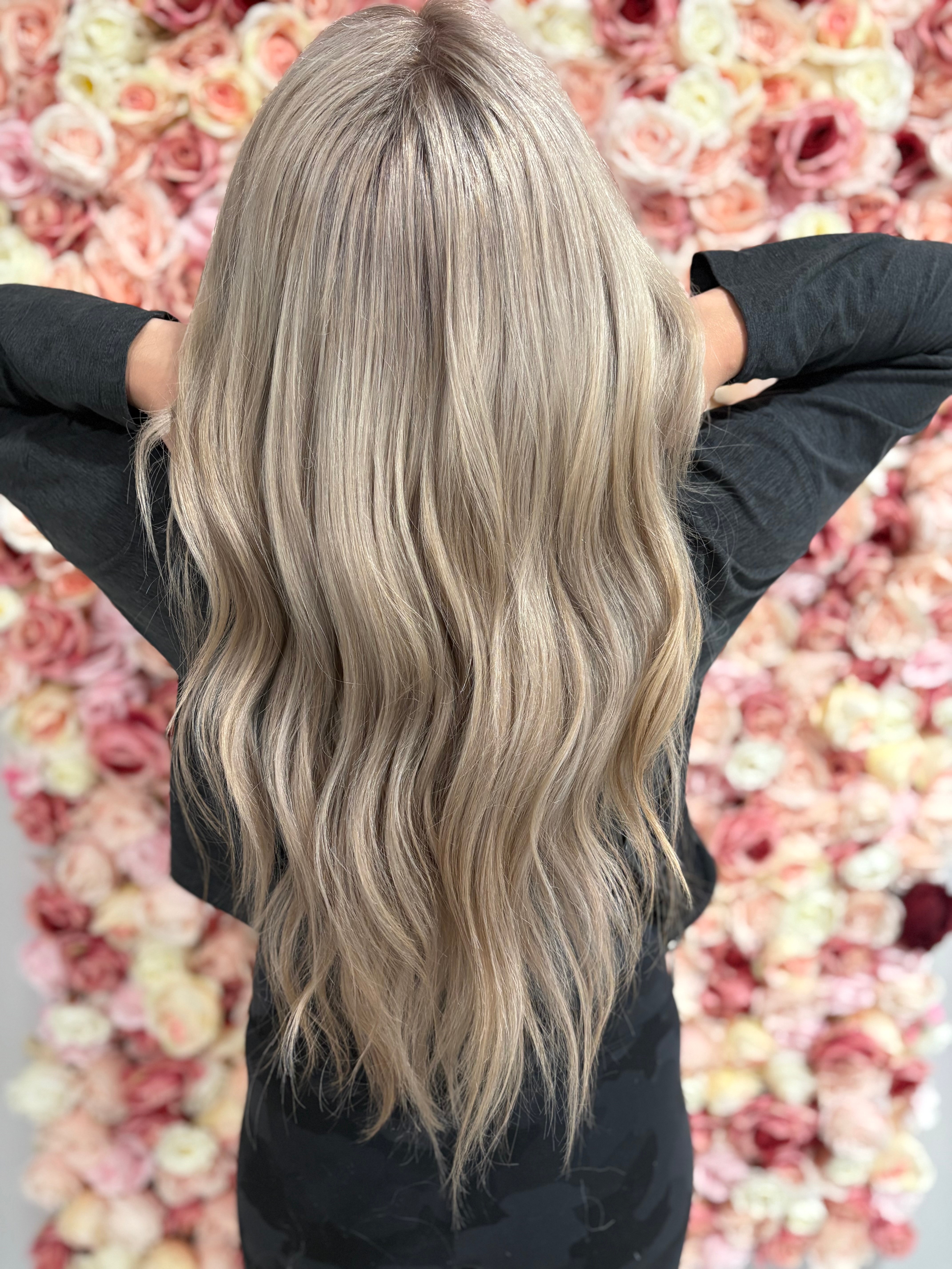 Back view of a person with long, wavy, platinum blonde hair against a pink floral background.