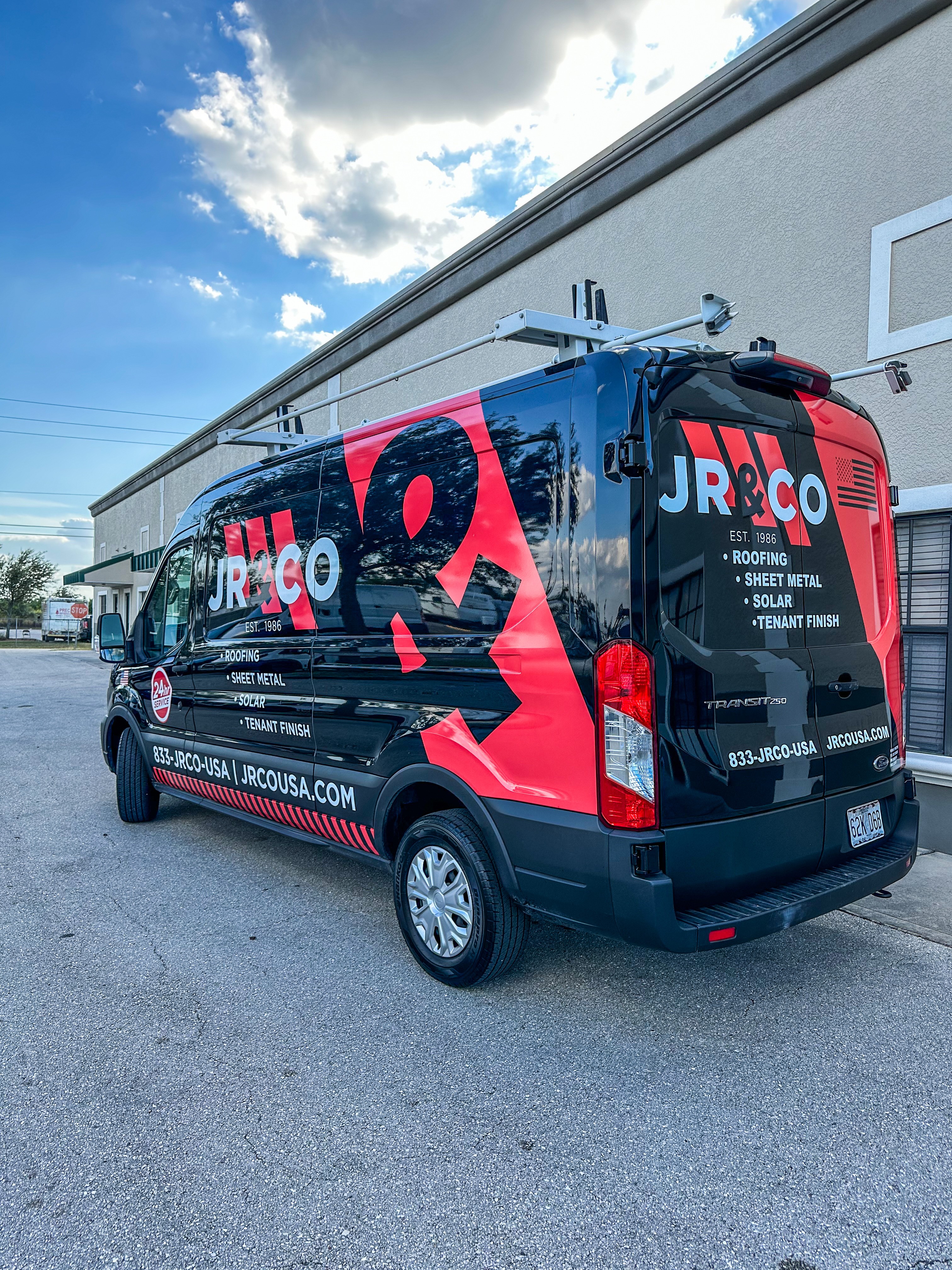 Black van with red and blue graphics parked outside a building under a partly cloudy sky.