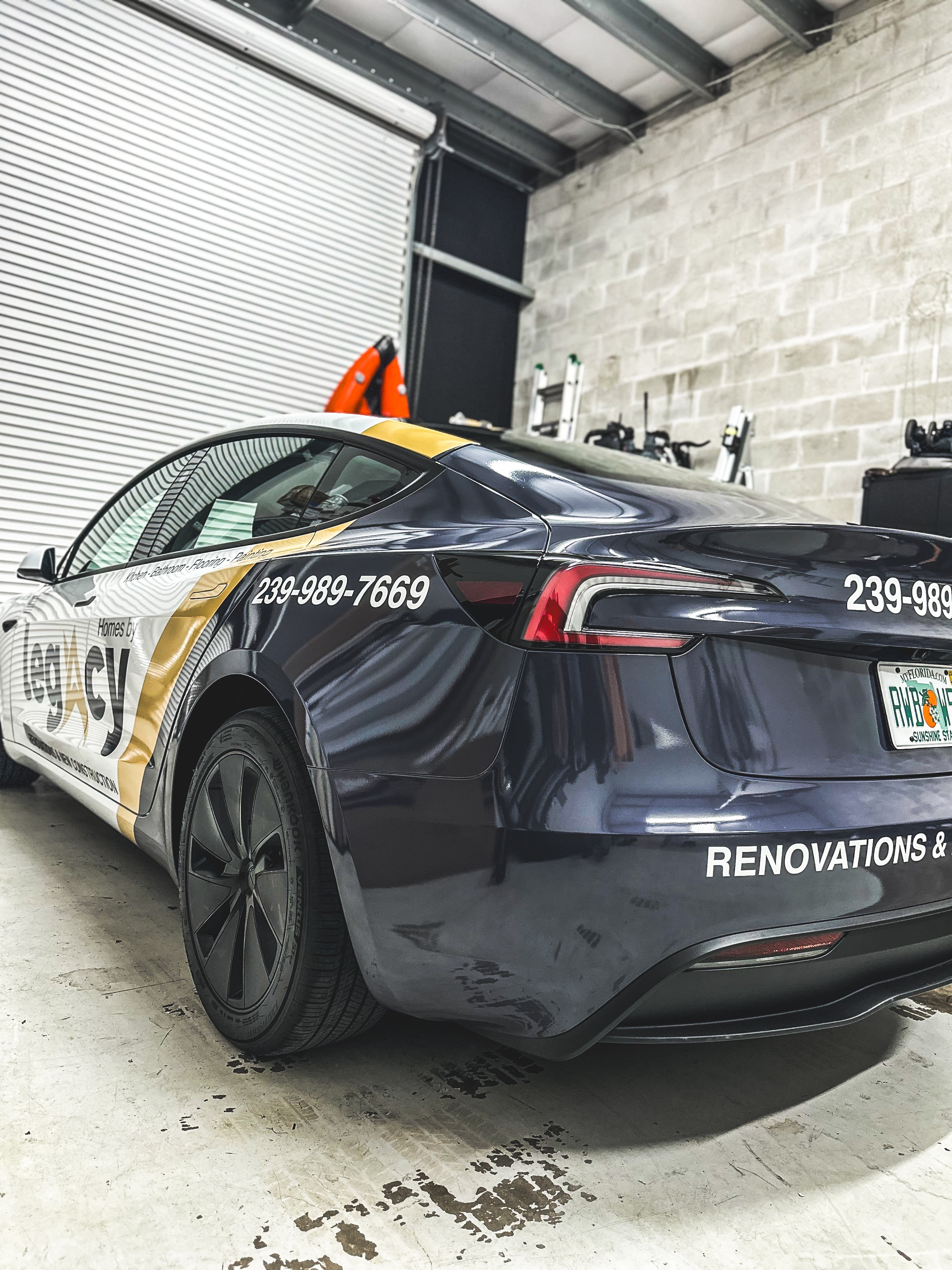 Black police car with white and yellow markings parked inside a garage, with equipment on the wall behind.