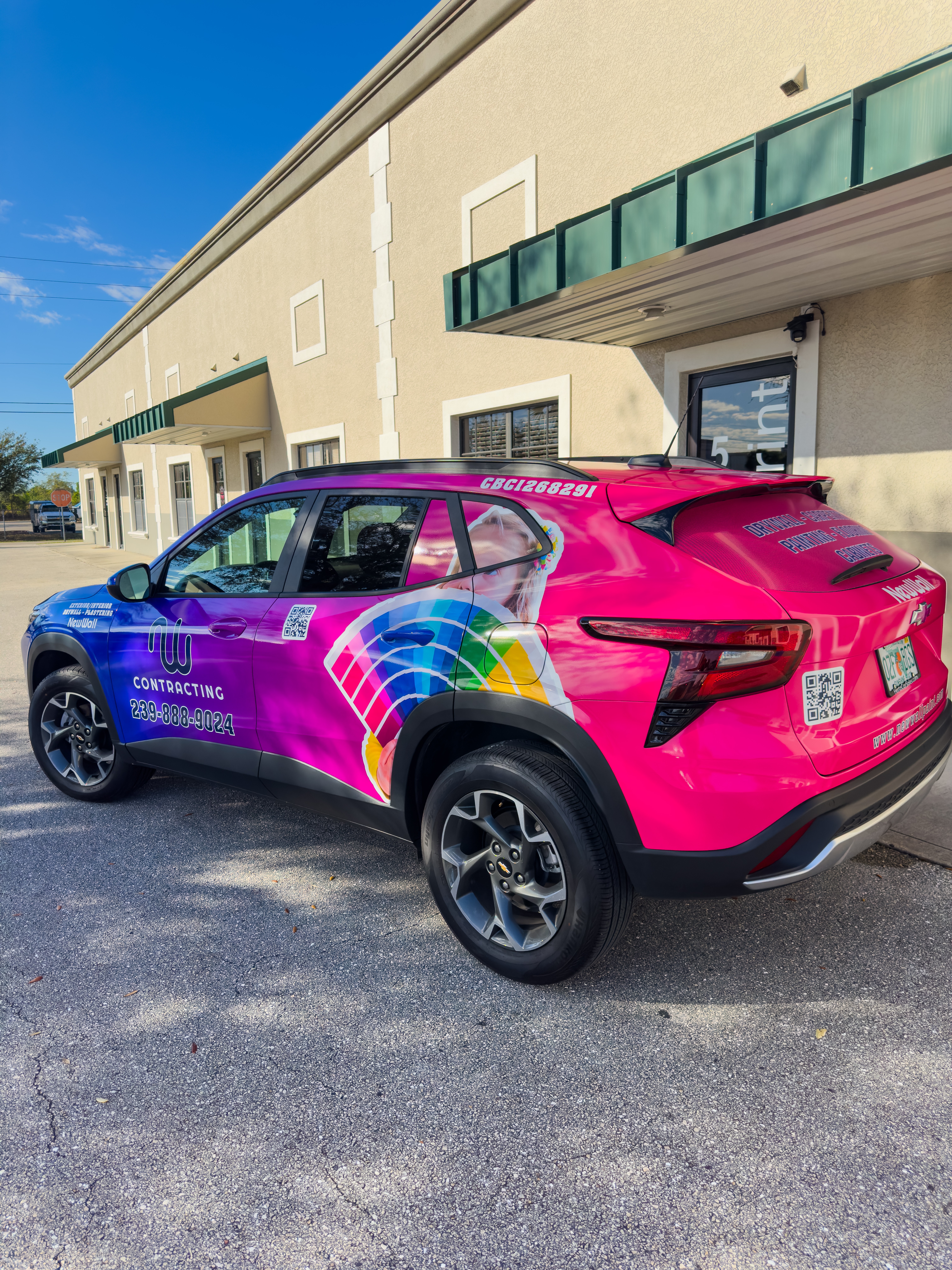 Colorful vehicle with graphics parked outside a beige building with a balcony, under a blue sky.