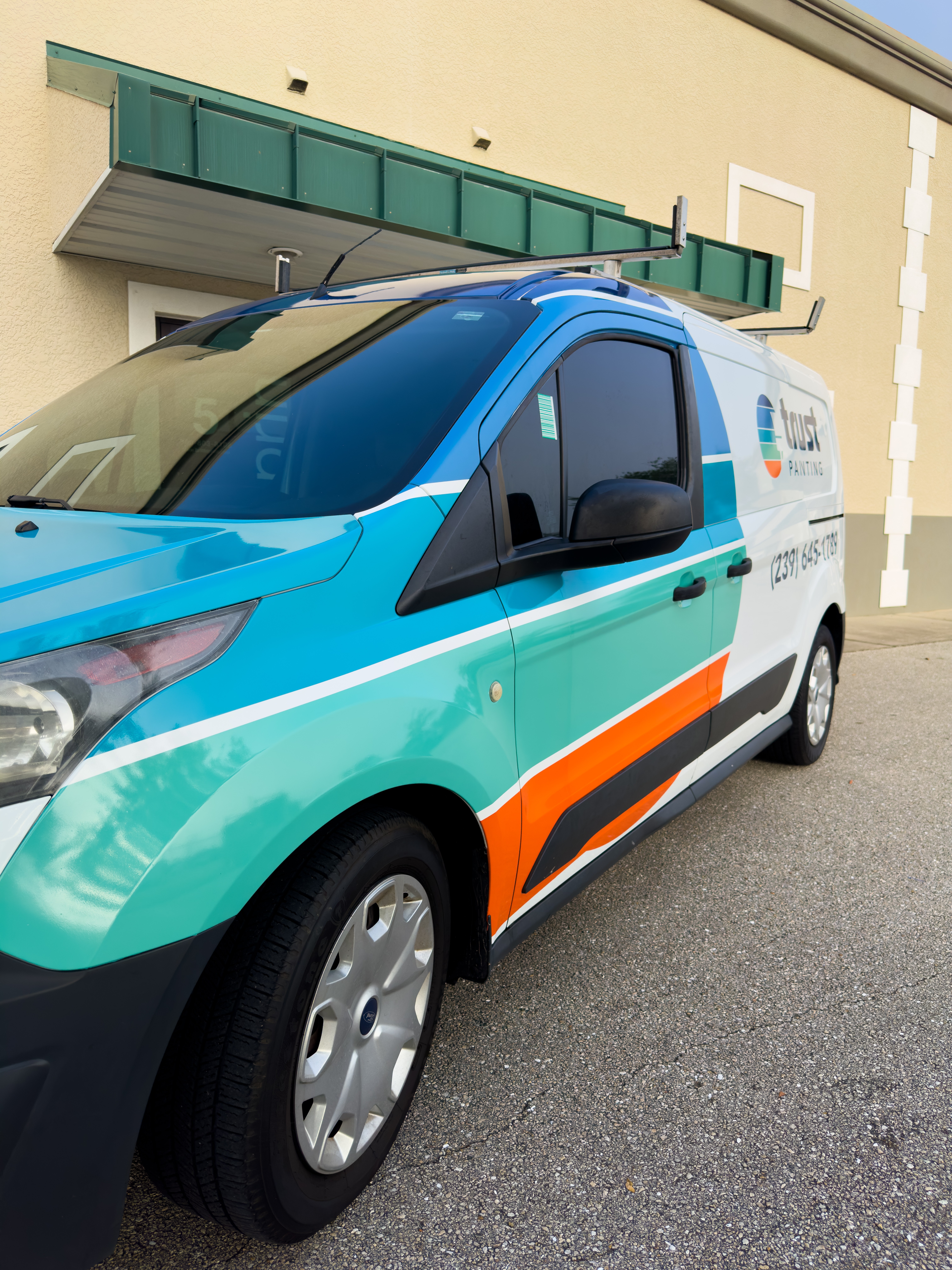 Colorful service van parked on street with building in background, featuring blue, white, orange, and teal design elements.