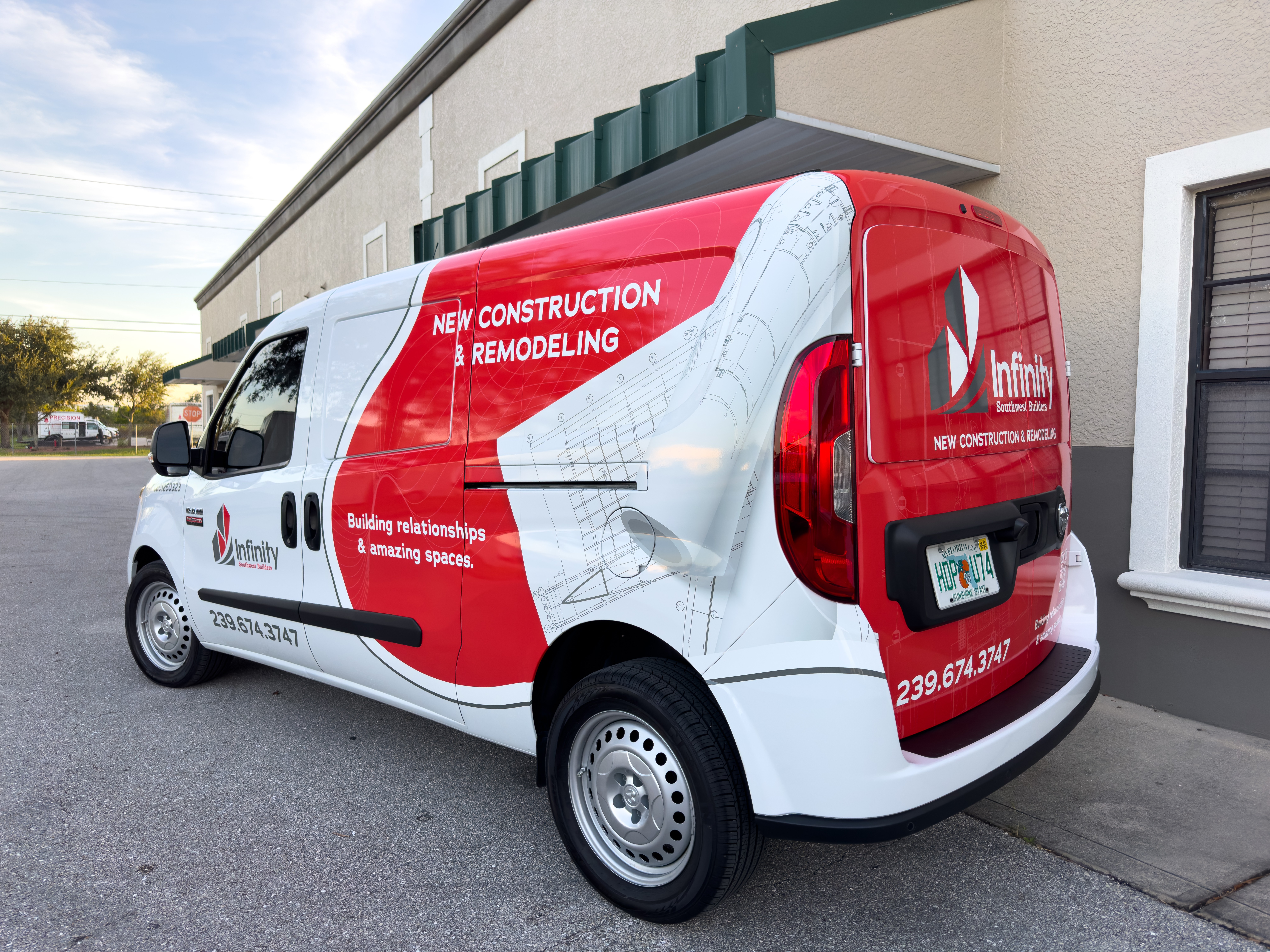 White and red construction and remodeling van parked outside a building with a window, advertising services on the side and back.