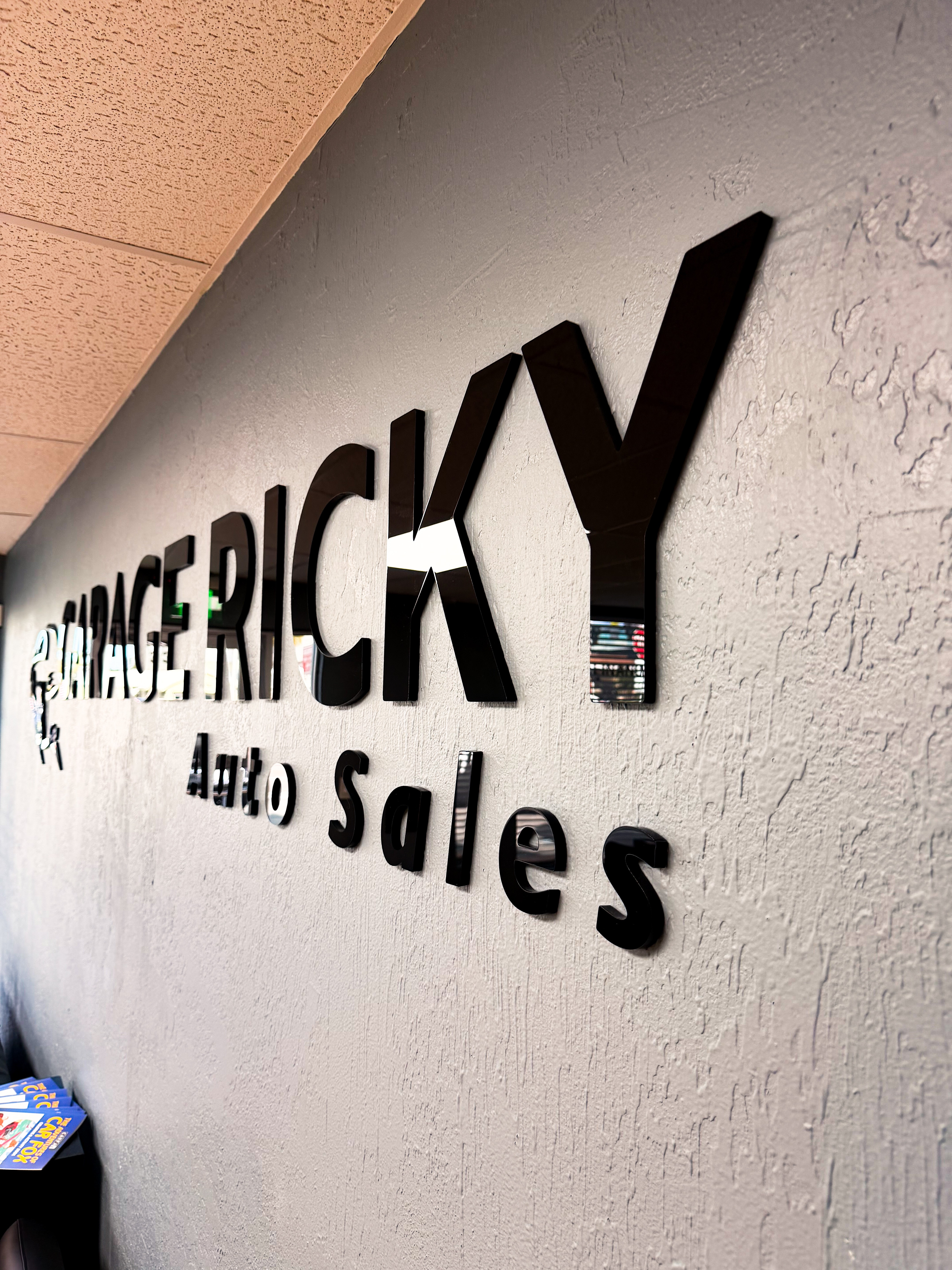 Wall sign with large black letters reading 'RICKY' and smaller text below, in an indoor setting.