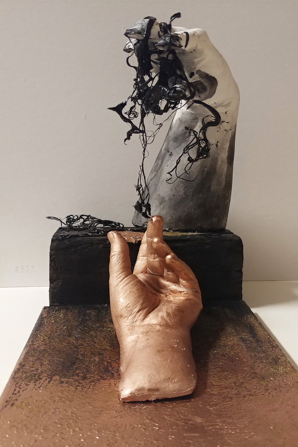 Sculpture of a head with tangled black hair, a hand holding a string, and a base with textured surface.