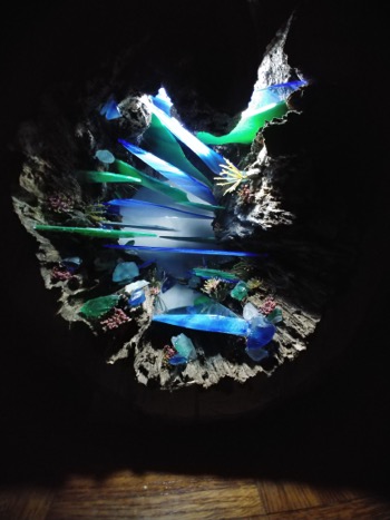 View of colorful kayaks and people in a cave with a small opening, illuminated by natural light, with water reflections.