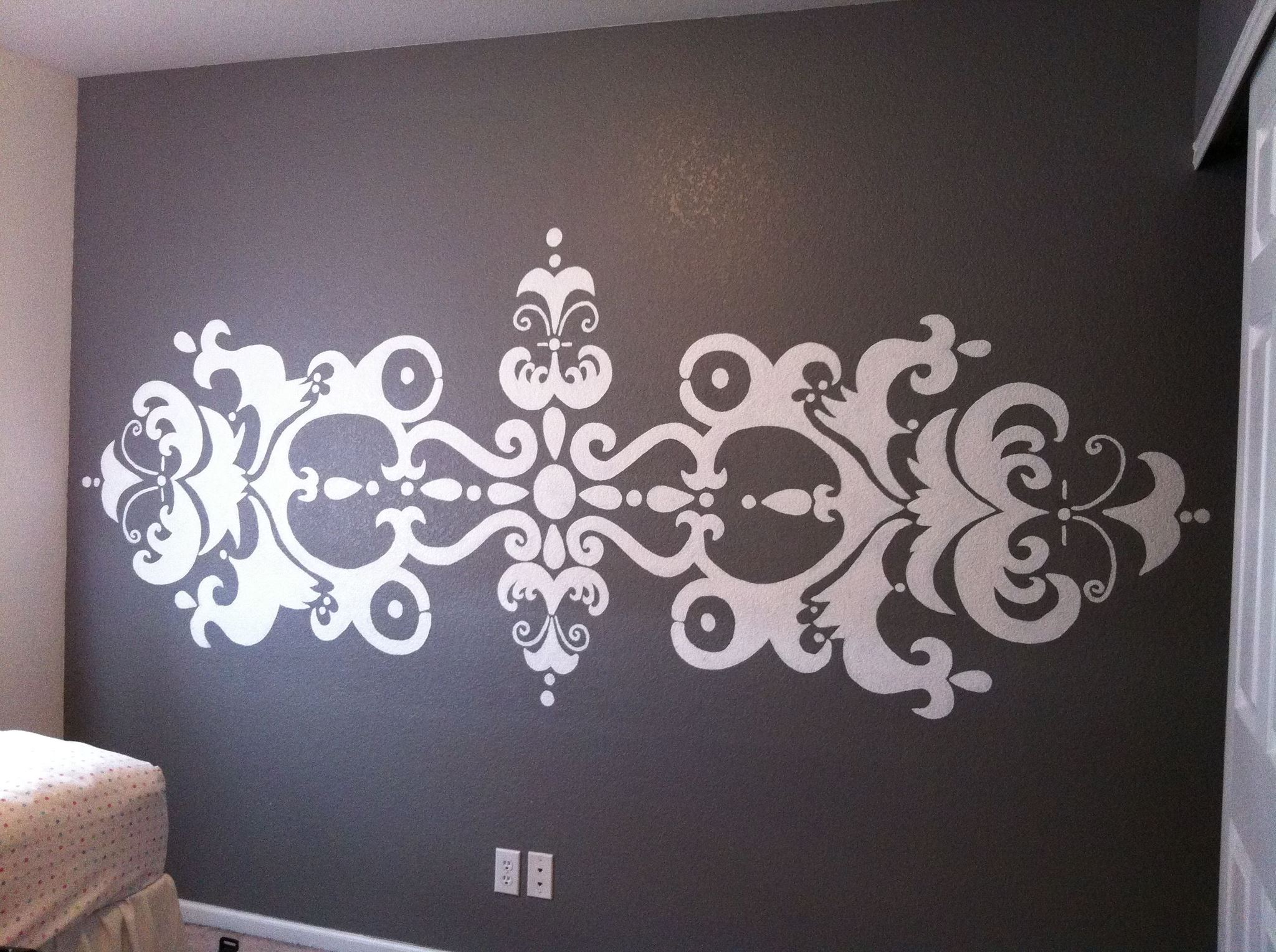 Decorative white symmetrical wall decal on dark wall with intricate floral and scroll patterns.