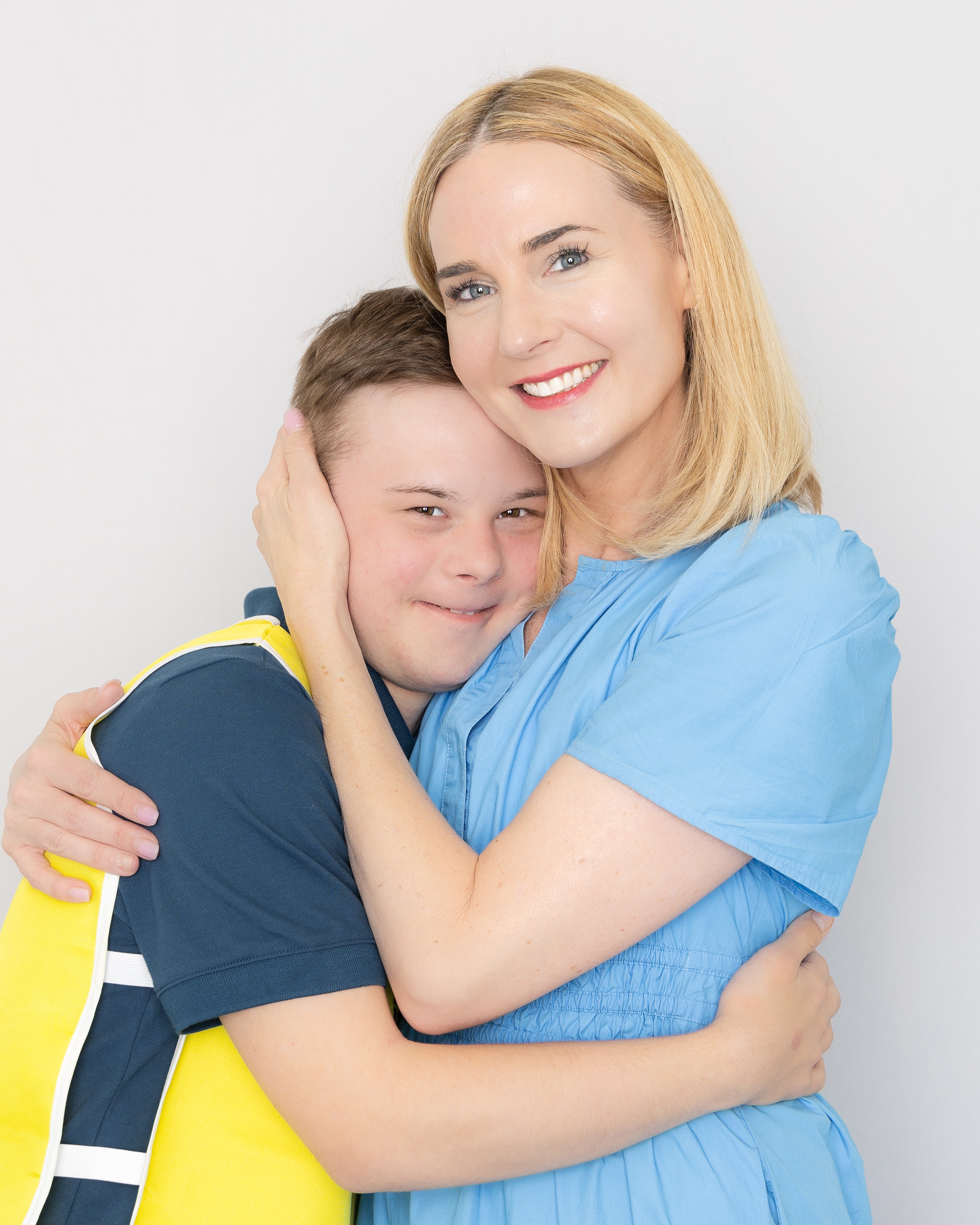 Woman and boy hugging, smiling, against a plain white background.