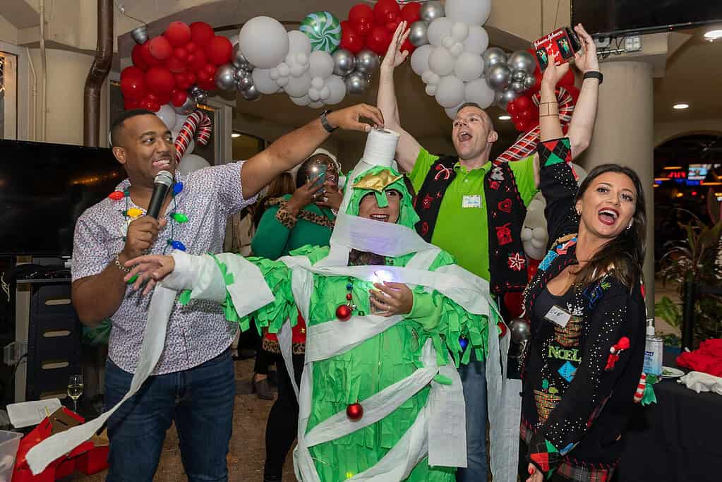 Group of people celebrating with balloons and decorations, some holding microphones and taking photos, in a festive setting.